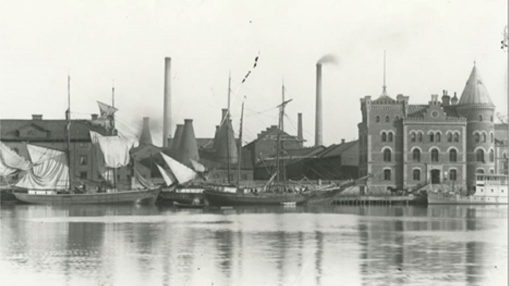 Arkivfoto av Gustavsbergs hamn med fabriken och segelfartyg.